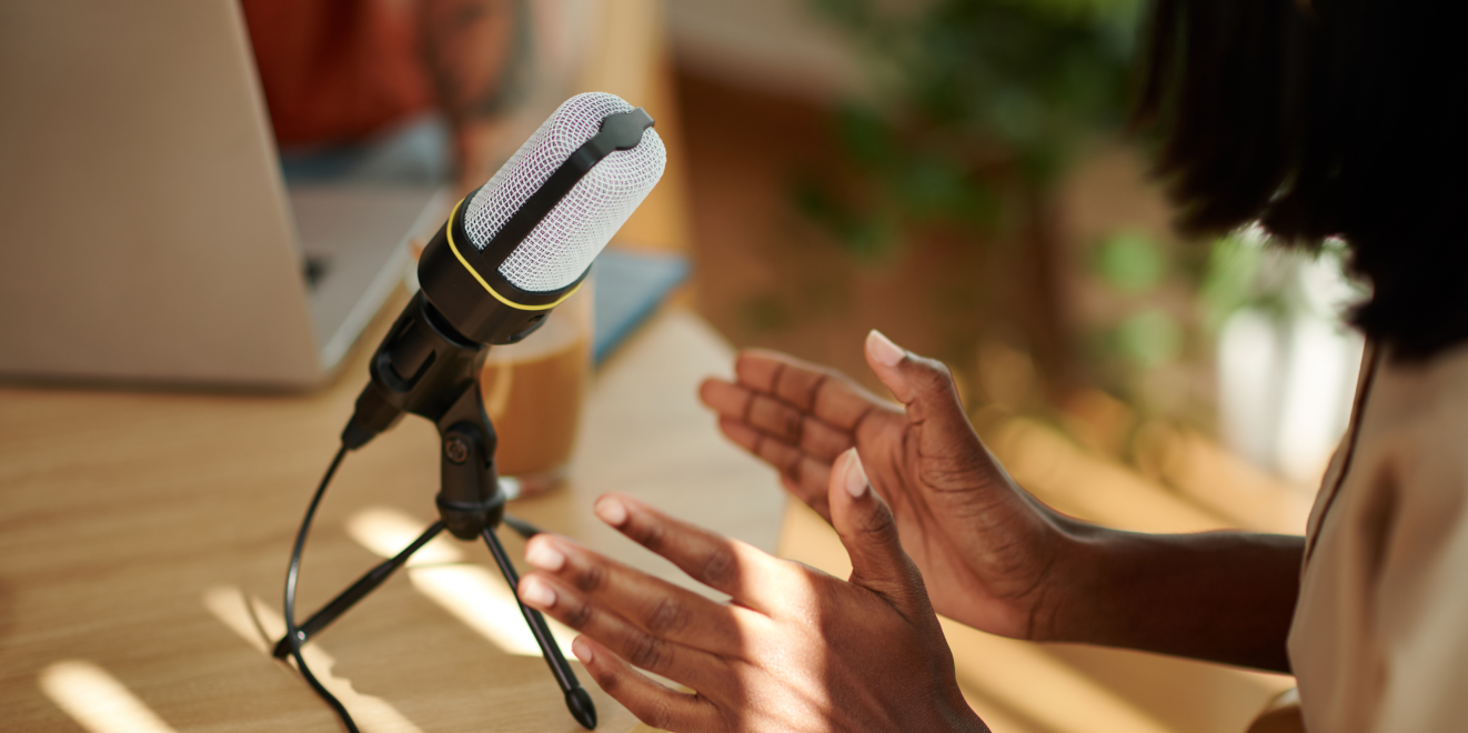 A woman holding a microphone in front of a laptop, speaking passionately.