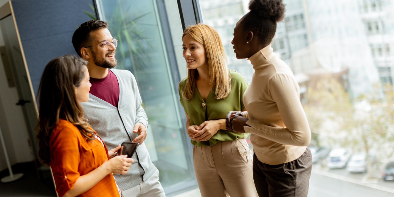 Four people smiling and having a conversation in an office building.